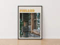 A framed travel poster of Finland leaning against a white wall on a light wood herringbone floor. The poster features a rustic log cabin window with the word 'FINLAND' in bold tan letters at the top.