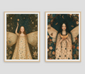 Two framed art prints featuring fairy-like female figures in ornate dresses against dark celestial and floral backgrounds, displayed side by side on a light gray wall.